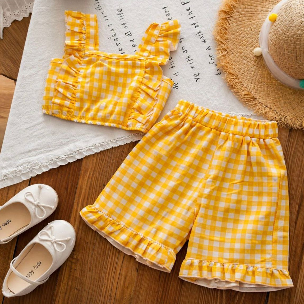 Yellow checkered outfit with shorts and top on a wooden surface with shoes and a hat.