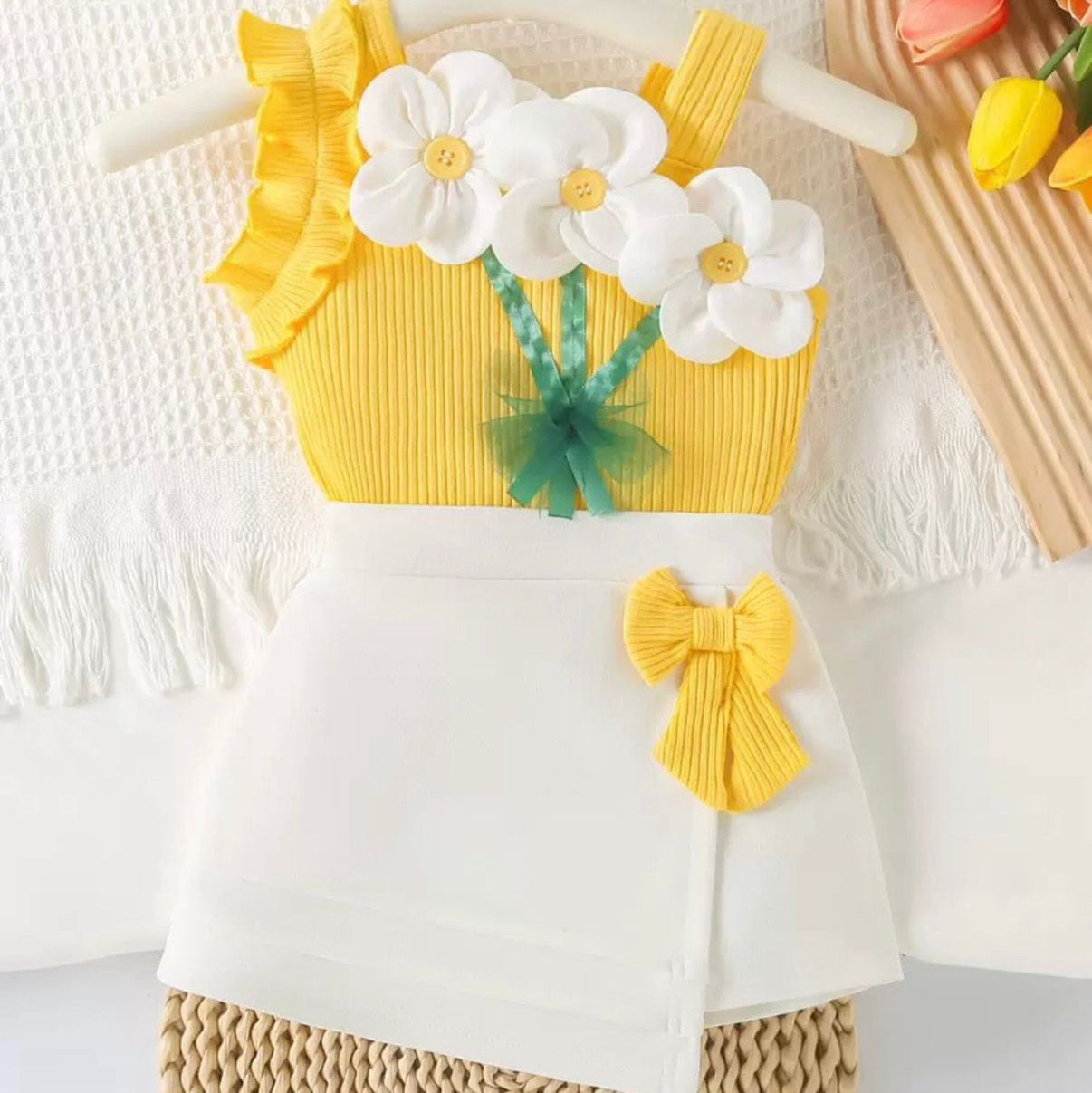 Children's outfit with yellow top, white skirt, and floral design on a textured surface.