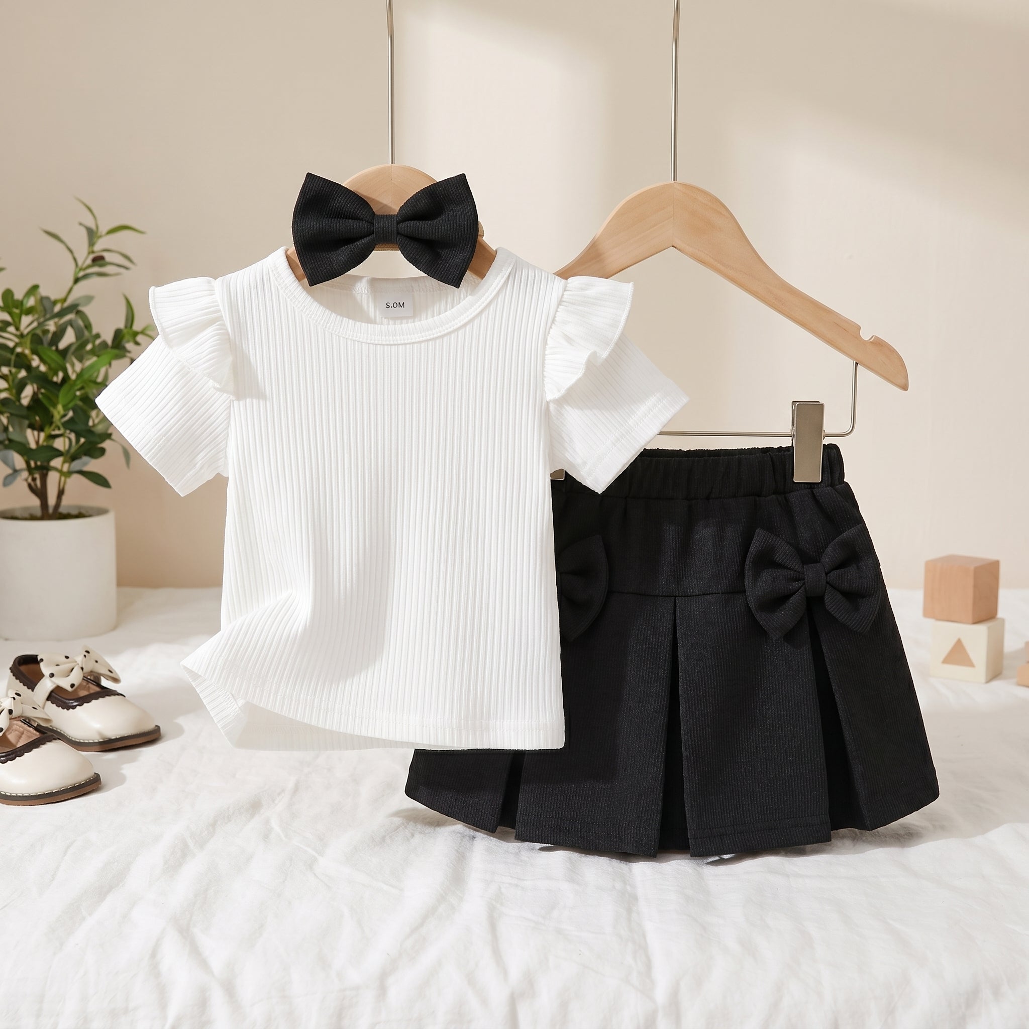 White ruffled shirt with black bow and black pleated skirt with black bow on a white surface.