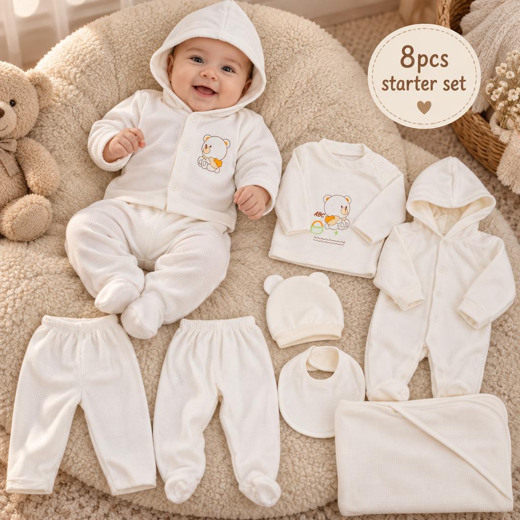 White newborn 8-piece bear starter set flat lay with hooded cardigan, printed top, hooded footed romper, two trousers, cap, bib and blanket.