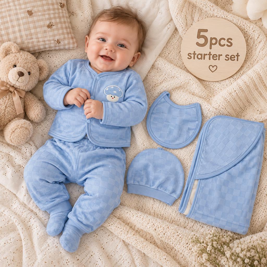 Blue newborn 5-piece quilted bear starter set styled on a baby, showing the front-open bear patch top, matching footed trouser, cap, bib and folded blanket.