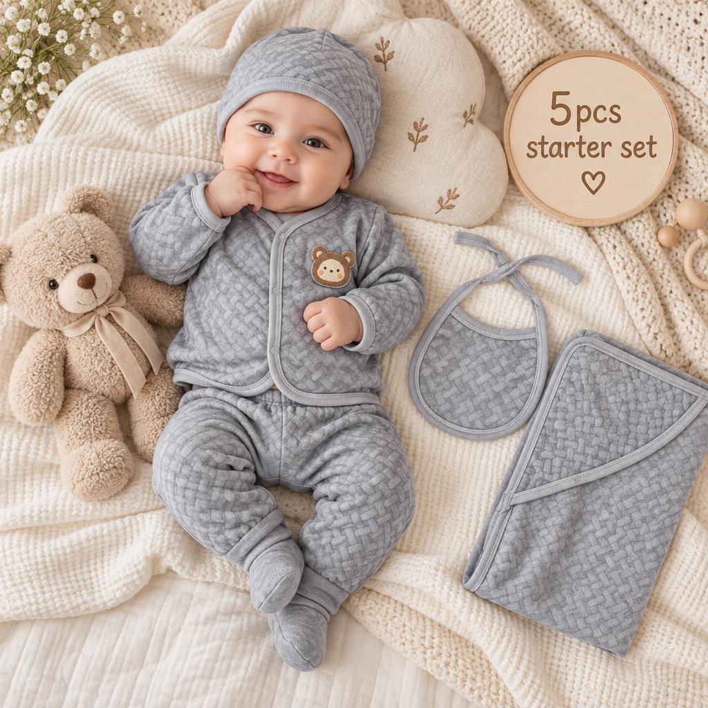 Grey newborn 5-piece quilted bear starter set in a styled flat-lay scene, featuring the textured front-open top, matching trouser, cap, bib and quilted blanket.