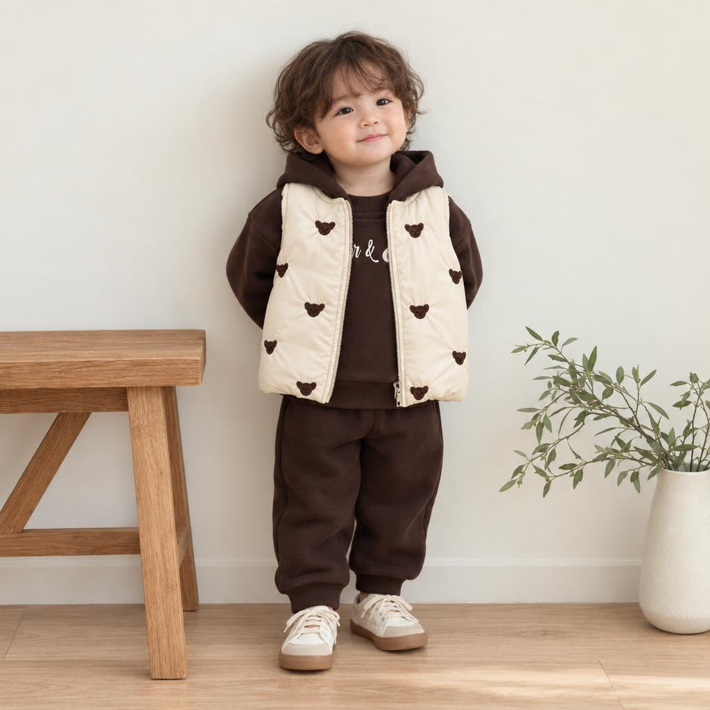 Toddler modelling the Dark Brown hooded sweatshirt and cuffed joggers with a Cream padded waistcoat decorated in Dark Brown bear faces.