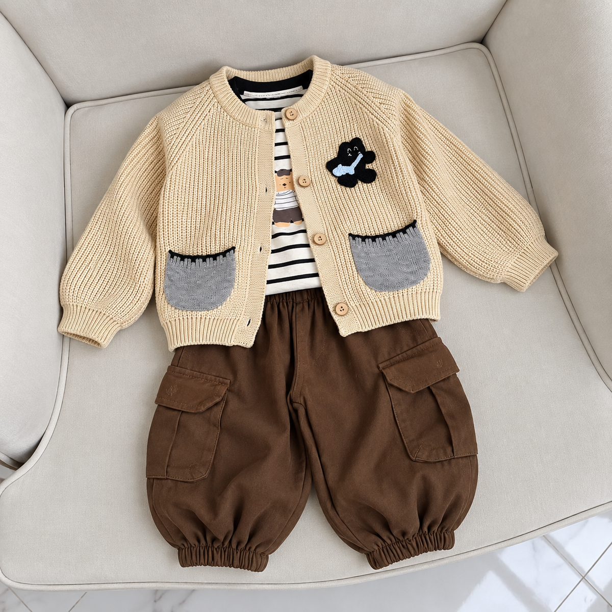 Beige knit-look button cardigan, striped shirt and Brown cargo trouser 3-piece boys suit laid flat on a cream sofa, showing contrast Grey pockets and chest applique.