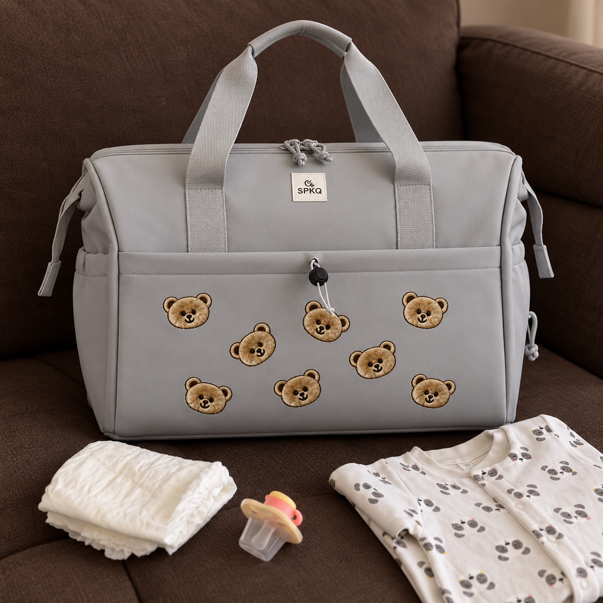Grey teddy bear easy carry mommy bag displayed on a sofa with a large front zip pocket and teddy bear face decoration