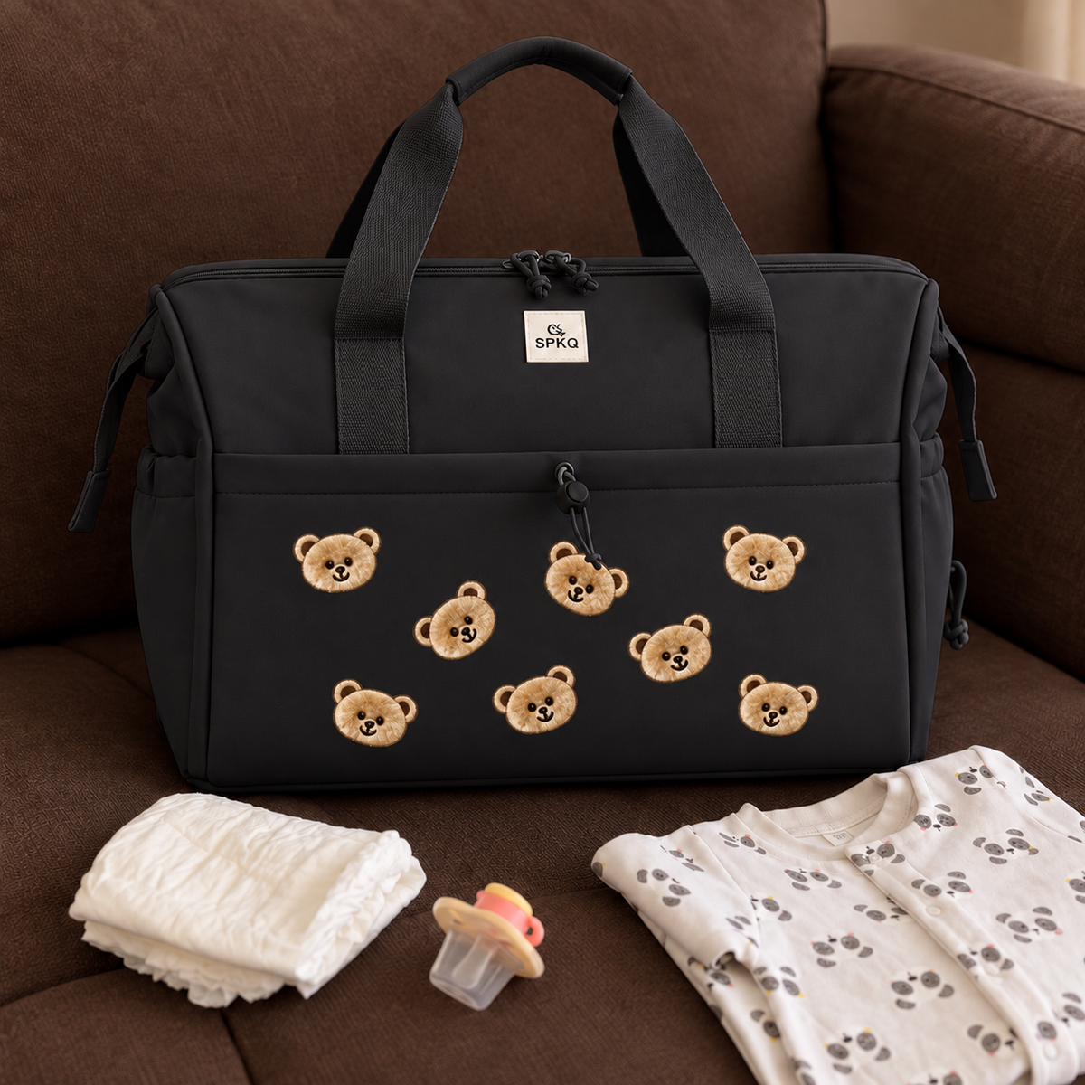 Black teddy bear easy carry mommy bag displayed on a sofa, featuring tonal handles, side zip sections and bear face appliques