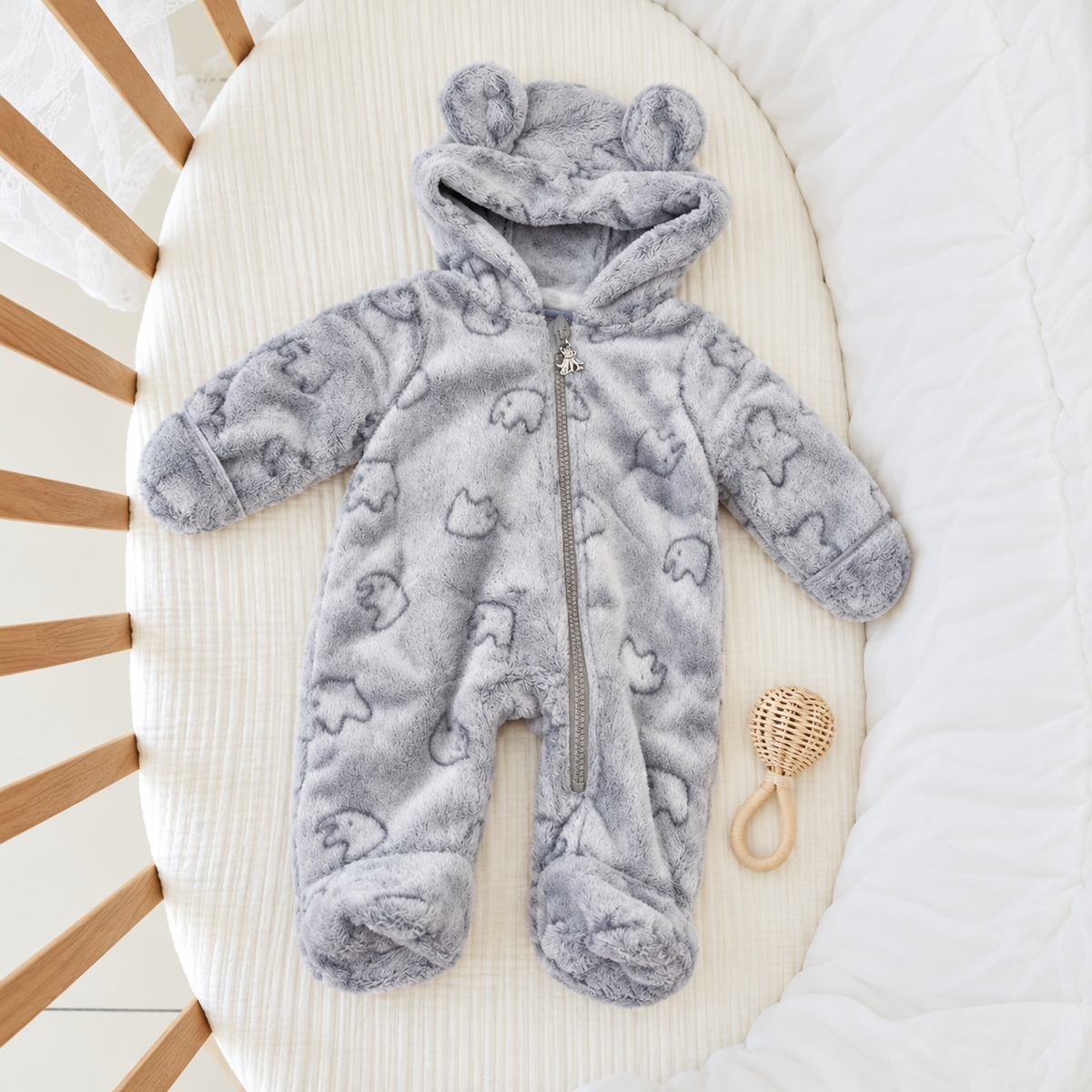 Grey shaggy baby romper displayed flat in a cot, with small outlined animal motifs, a bear-ear hood, centre zip opening and covered feet.