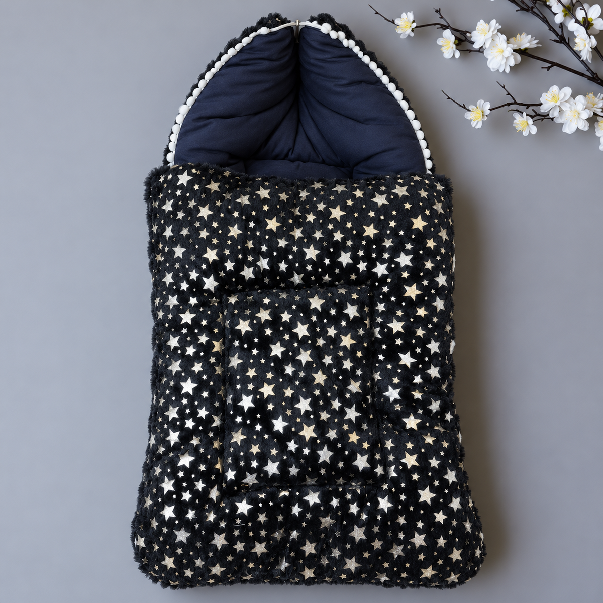 Blue baby shaggy carry nest shown flat lay, with White and Gold-tone star print, deep Blue padded hood and White pom-pom trim.