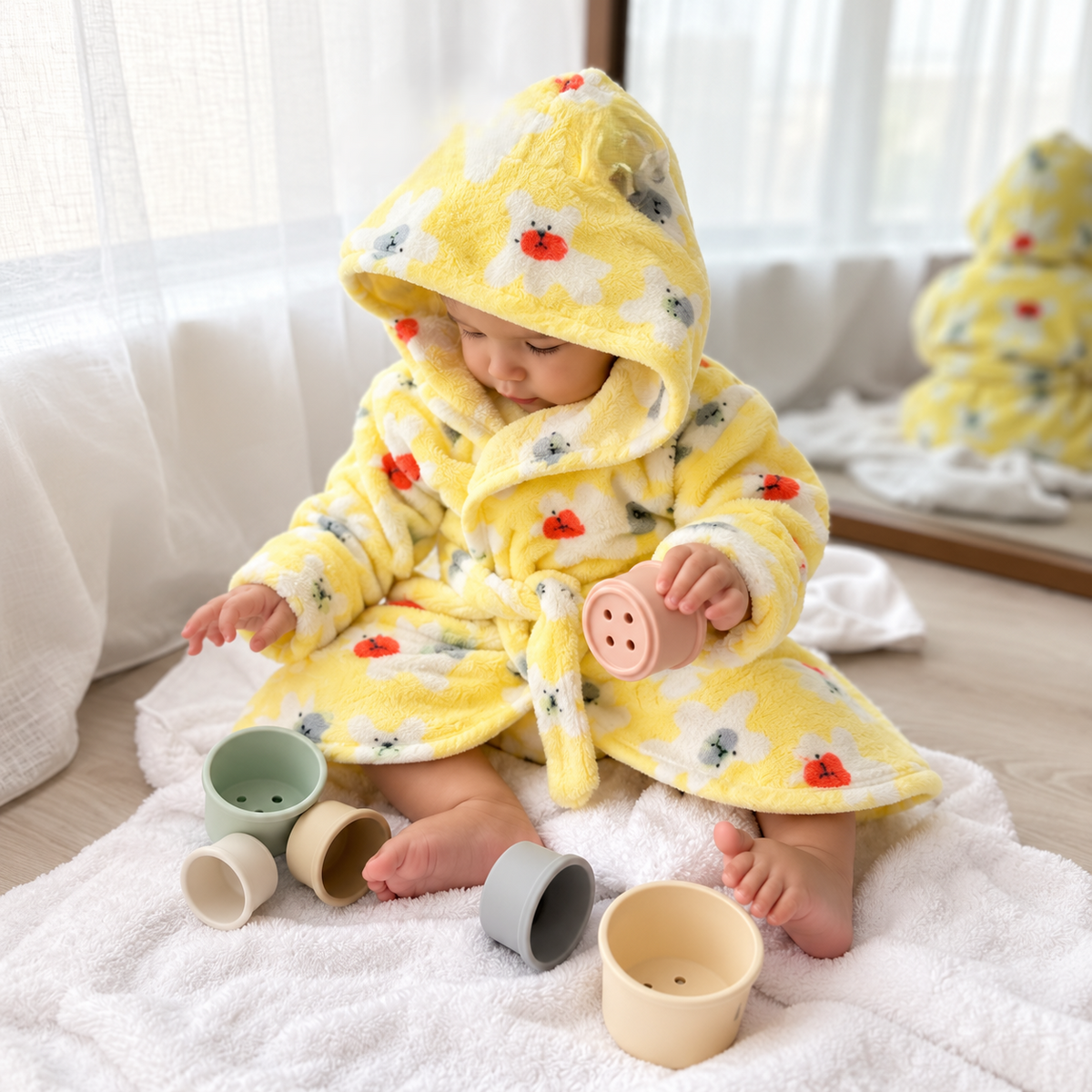 Baby wearing a Yellow plush hooded bath robe with White flower, small animal and red ladybird-style print, tied at the waist.