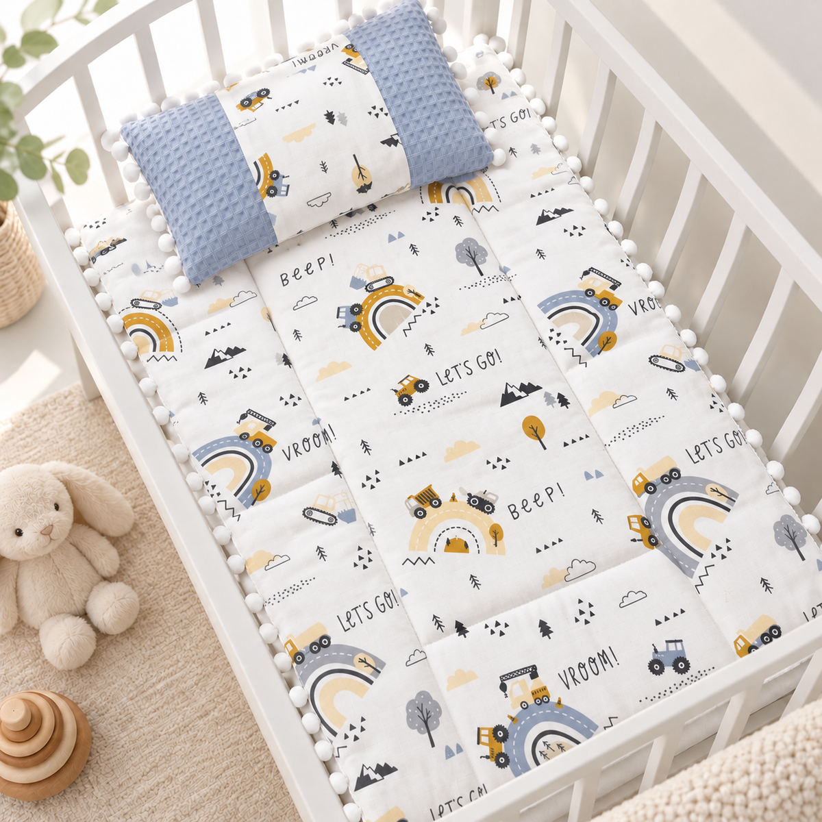 Light Blue vehicle and rainbow printed baby sleeping sheet with a matching Blue textured-side pillow, shown in a White crib.