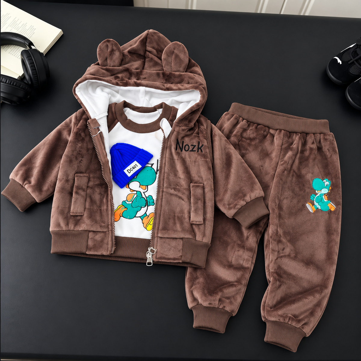 Dark Brown velvet baby 3-piece suit displayed flat, featuring a White-lined ear hood, colourful dinosaur graphic shirt and matching jogger trousers.