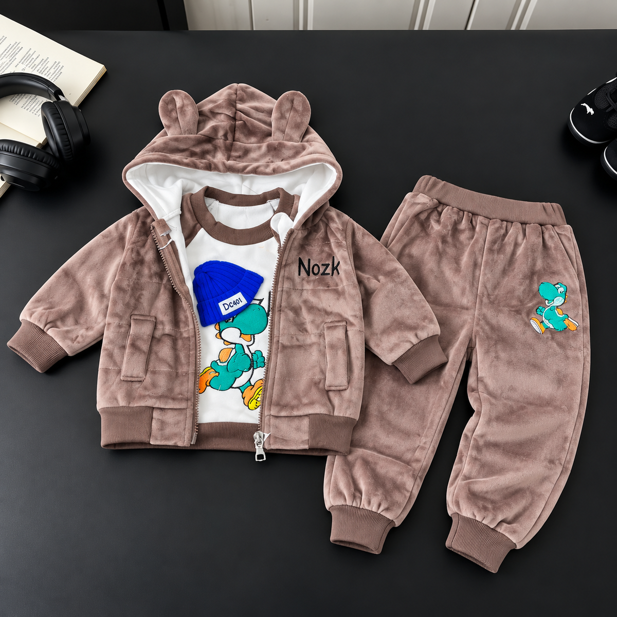 Mauve velvet baby 3-piece suit laid flat, showing an ear-detail zip hooded jacket, White cartoon dinosaur shirt and matching cuffed trousers.