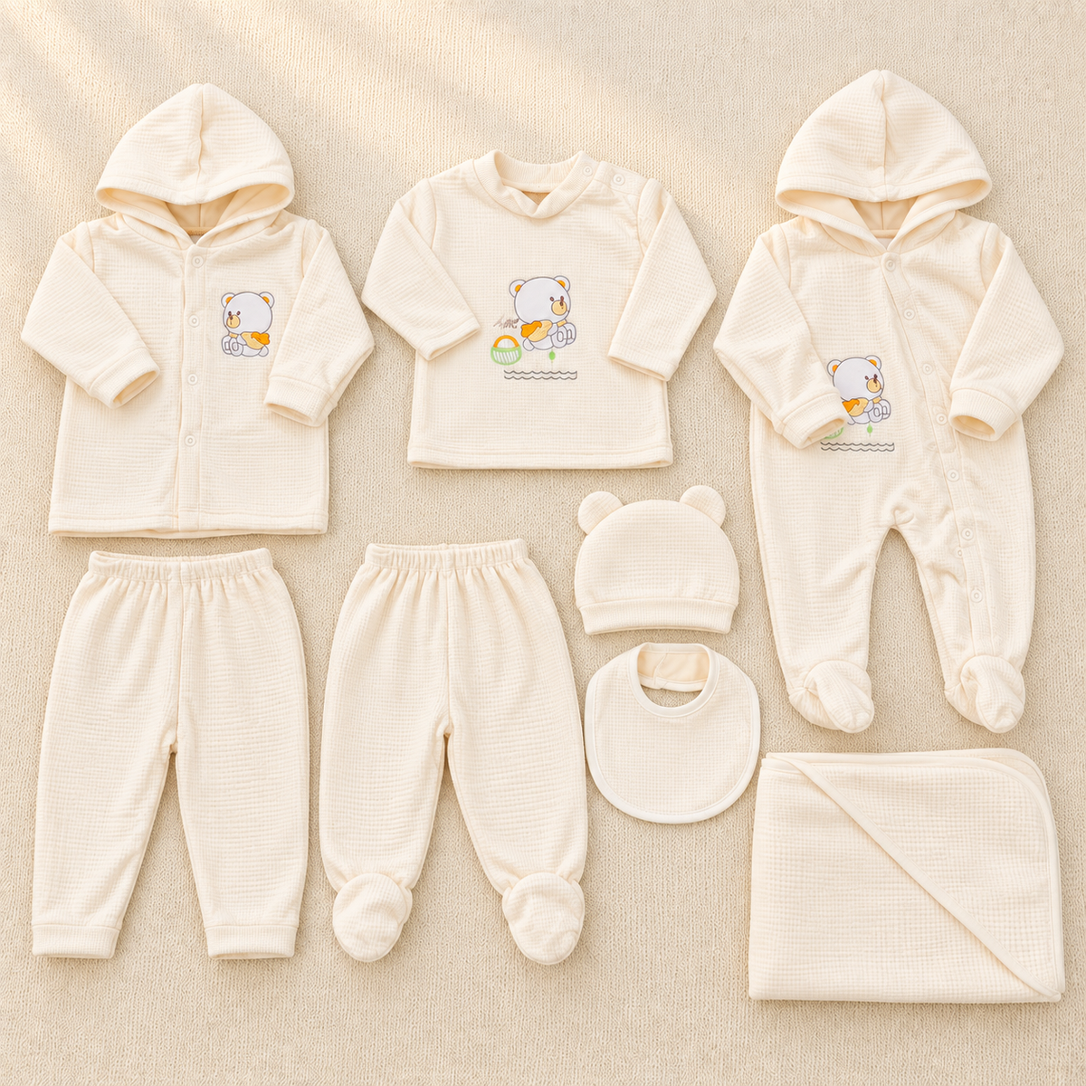 Cream bear waffle newborn starter set flat lay showing the hooded cardigan, ABC bear top, hooded footed romper, cap with ears, bib and blanket.