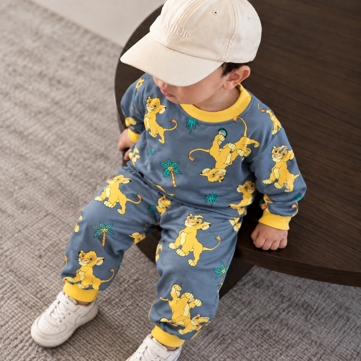 Toddler boy wearing the Blue-Grey lion and palm-tree print shirt and trouser set with bright Yellow ribbed trims.