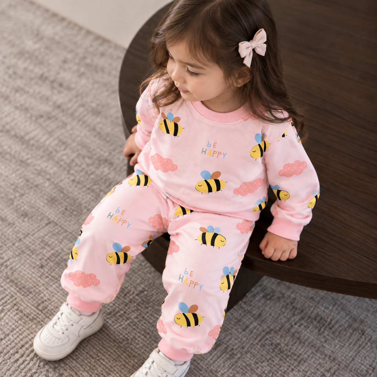 Toddler girl wearing the pink bee print shirt and trouser set, featuring yellow bees, pink clouds and Be Happy wording.