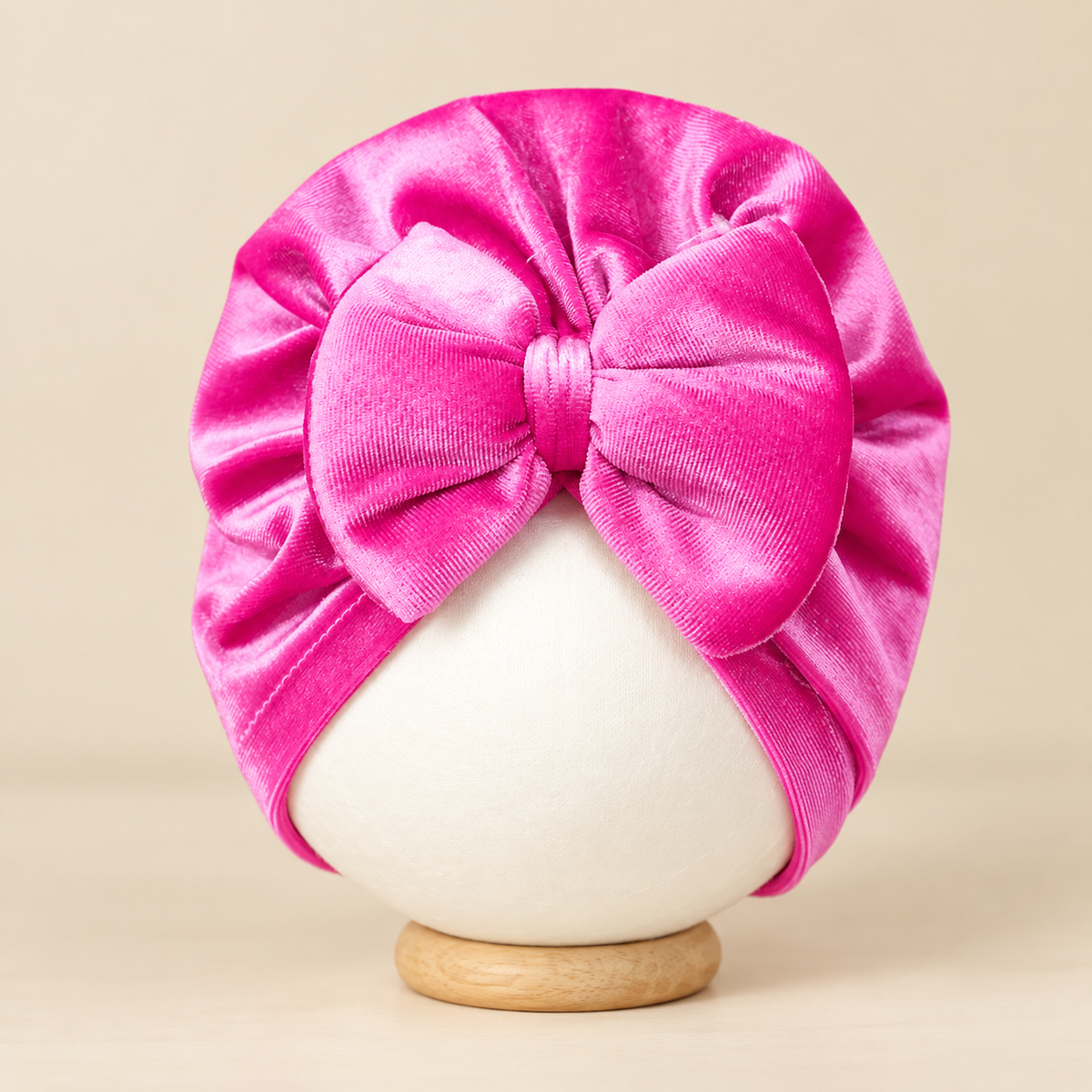 Bright Pink velvet baby turban cap on a mannequin display, with a ruched turban crown and oversized bow at the front.
