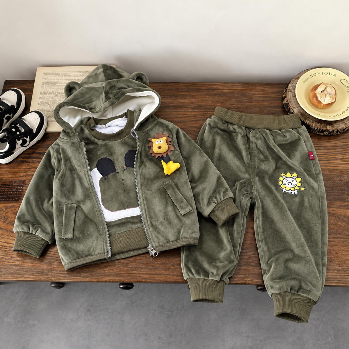Dark Olive kids 3-piece velvet suit flat lay featuring an animal-ear hooded zip jacket with lion applique, graphic shirt and cuffed trousers with flower patch.