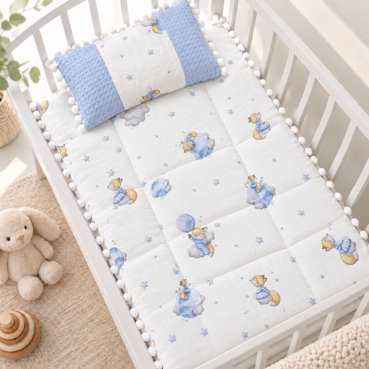 Blue teddy bear and star printed baby sleeping sheet with matching Blue textured-side pillow, displayed inside a White cot with pom pom edging.
