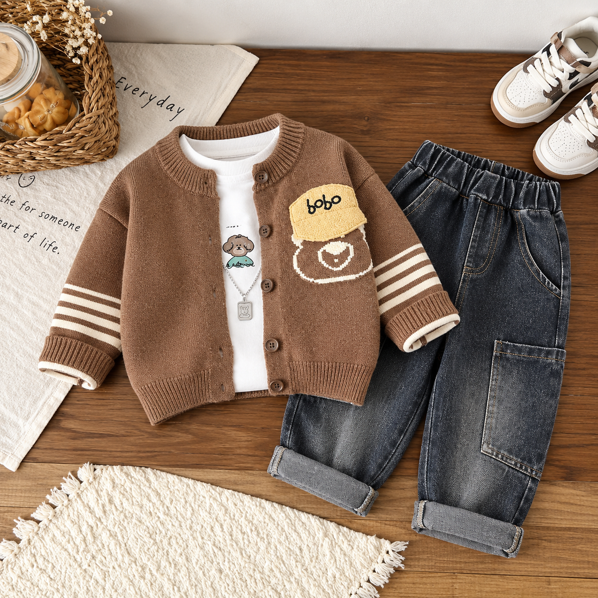 Flat lay of the Brown knit button cardigan with Bobo patch and bear pocket motif, White animal-print shirt and dark denim-look elastic-waist pants with rolled cuffs.
