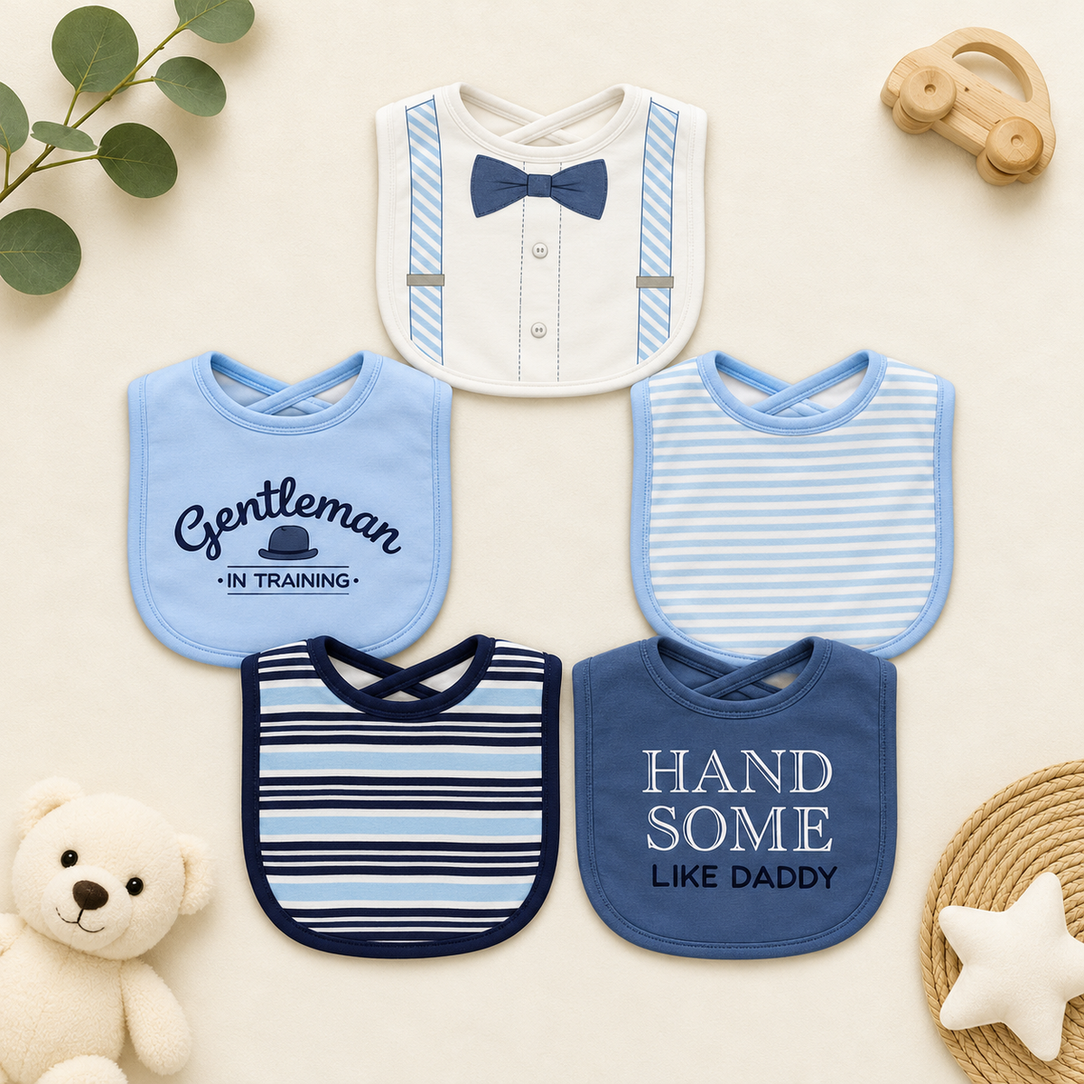 Five-piece baby gentleman bib collection arranged flat, showing Blue, White and Navy bibs with bow-tie, striped, Gentleman In Training and Handsome Like Daddy designs.