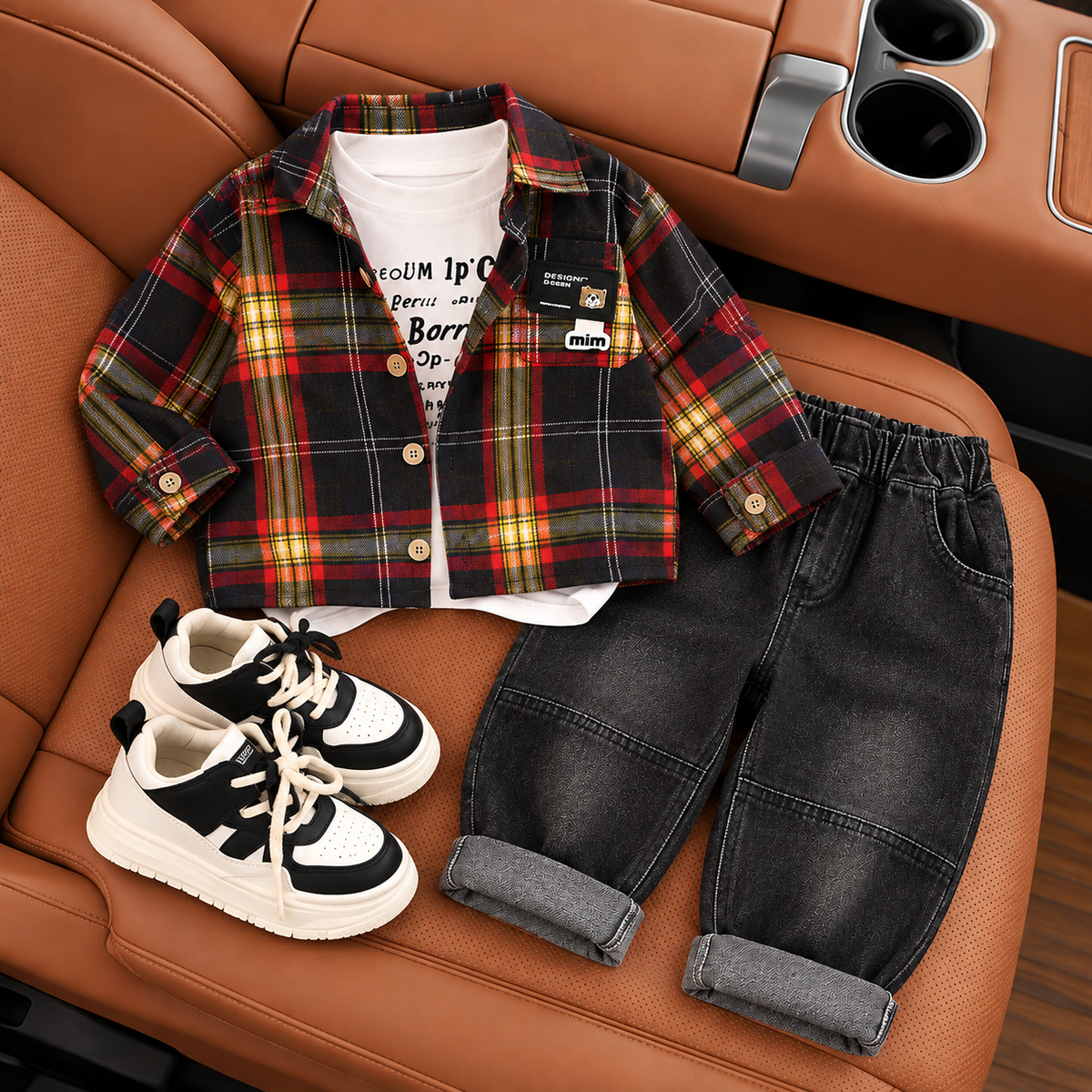 Black, Red and Yellow check boys button-front shirt with White printed inner shirt and washed Black cuffed denim-look trousers, shown as a flat lay on a tan car seat.