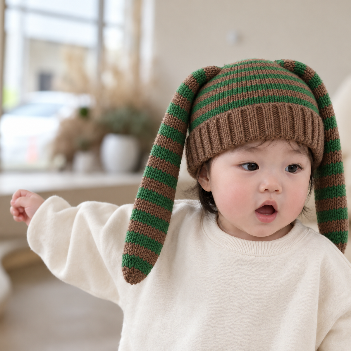 Toddler wearing a Green and Brown striped knit-look bunny ear winter cap with long floppy ears and a wide Brown ribbed cuff.