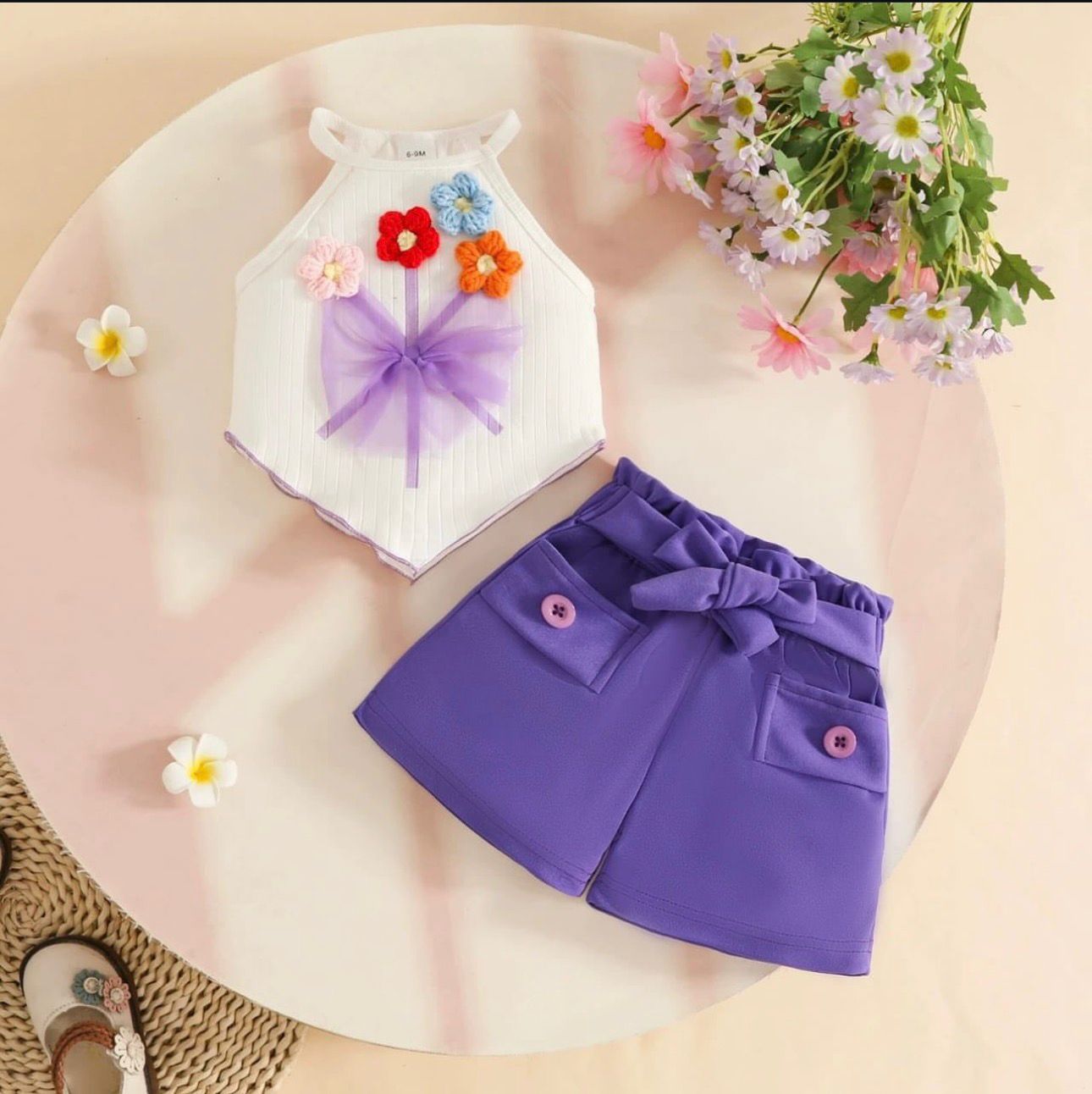 Purple shorts with a bow and white top with floral decorations on a pink surface.