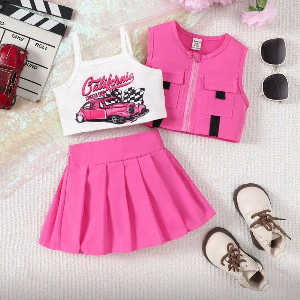 Pink outfit with tank top, skirt, and vest on a textured surface with flowers and car toys.