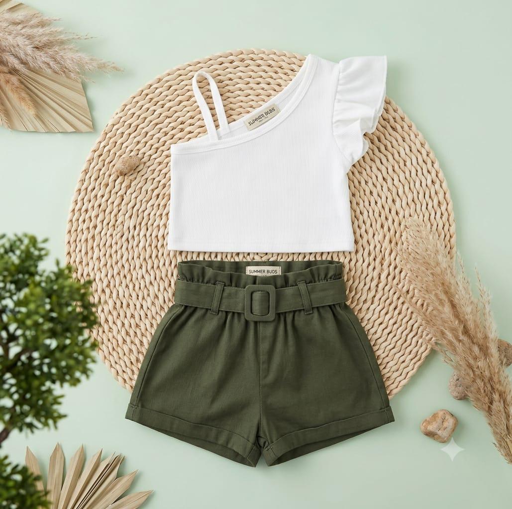 White top and green shorts set on a textured surface with plants around