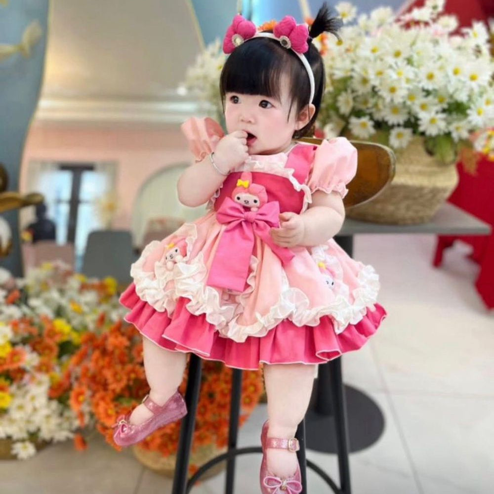 Child in a pink dress sitting on a stool with flowers and decorations in the background