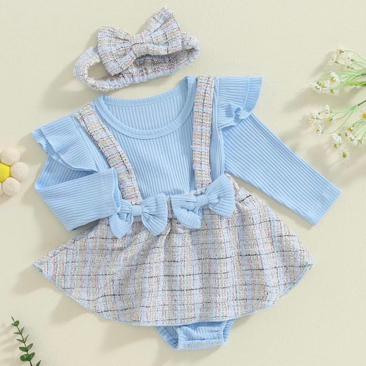 Baby outfit with blue top, plaid skirt, and headband on a beige background