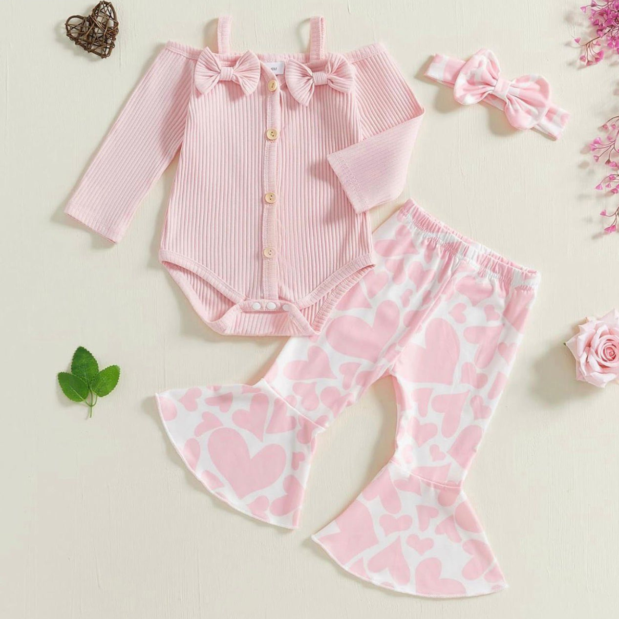 Pink baby outfit with long-sleeve top, heart-patterned pants, and headband on a light background.