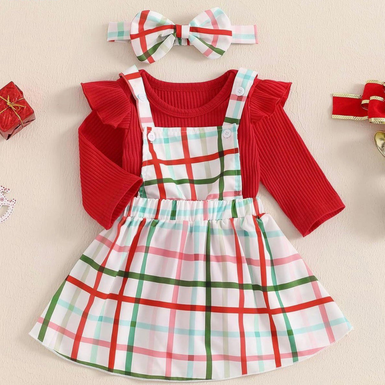 Children's outfit with red sweater, plaid dress, and headband on a beige background