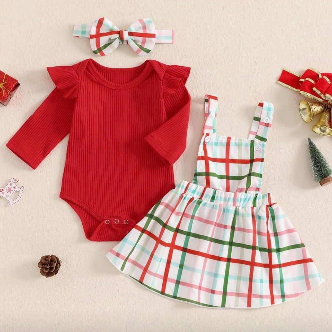Red baby bodysuit and plaid dress set with headband on a beige background
